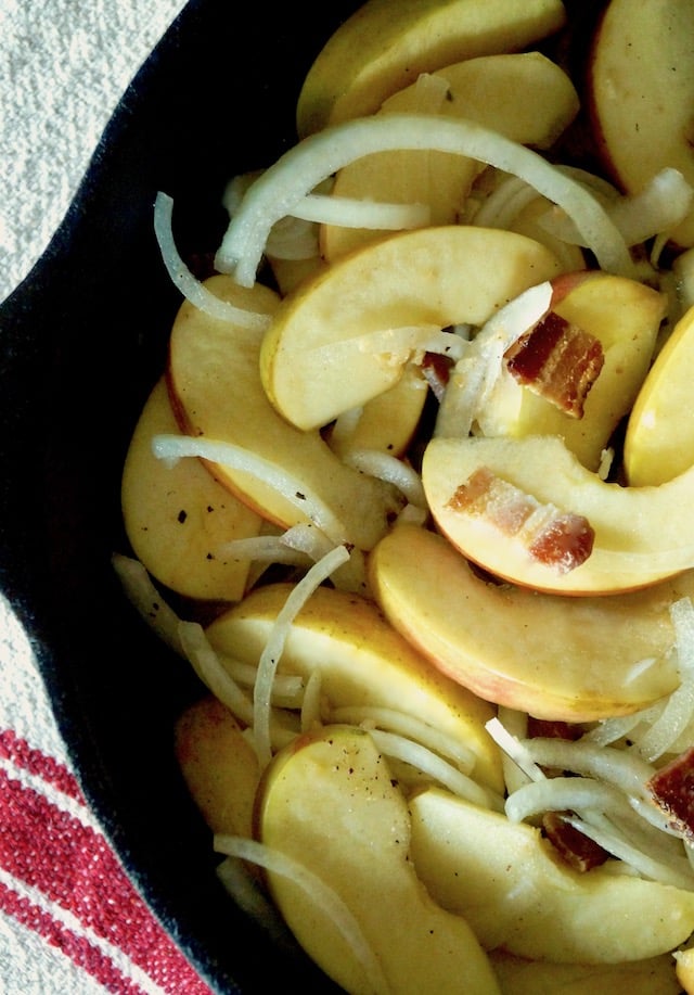 Apple slices with onion and bacon pieces in a cst iron skillet.