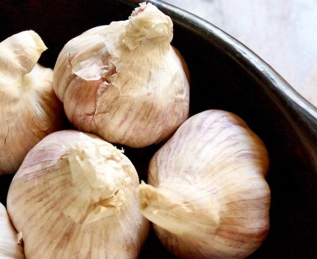 a few heads of purplish garlic in black bowl.