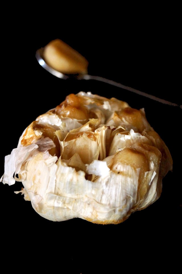 One roasted head of garlic with one clove in a tiny spoon behind it