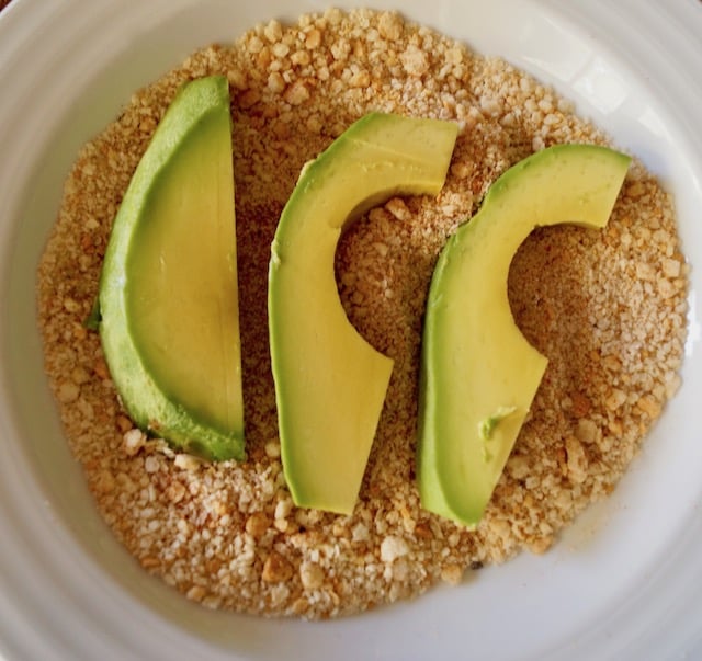 Three slices of avocado sitting on a gluten-free, spiced breadcrumb mixture.