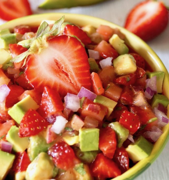 Strawberry Avocado Salsa recipe in a yellow-green bowl with half of a whole strawberry on top