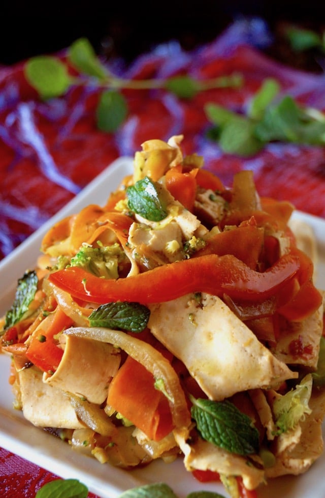 Close up of Vegetarian Mint Stir Fry Recipe wtih Tofu Noodles on a square white plate, with a red cloth beneath it.