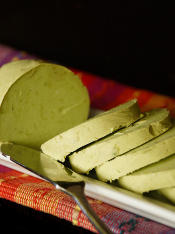 Round slices of Avocado Butter on a narrow plate with a spreader.