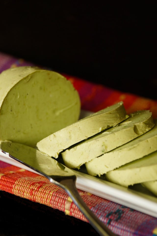 Round slices of Avocado Butter on a narrow plate with a spreader.