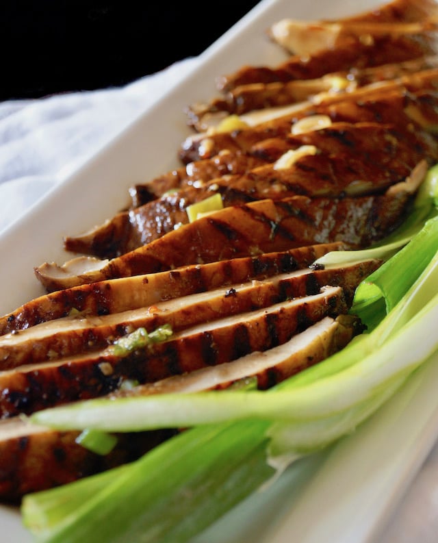 With grill marks showing, thinly sliced Marinated Grilled Portabello Mushrooms on a white plate with green onions.