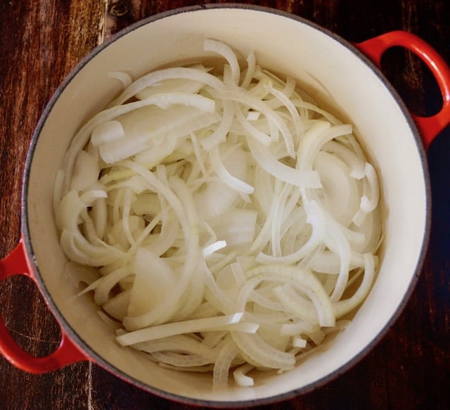 Thinly sliced onions in a large red-handled pot
