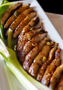 Close up of sliced Sliced Marinated Grilled Portabello Mushrooms on a white rectangulsr plate with green onions.
