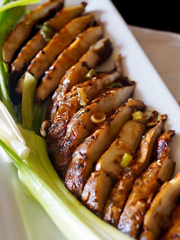 Close up of sliced Sliced Marinated Grilled Portabello Mushrooms on a white rectangulsr plate with green onions.