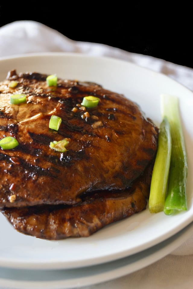 2 large whole Marinated Grilled Portabello Mushrooms on a white plate with chopped green onions on top.