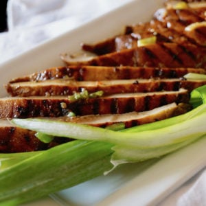 Sliced Marinated Grilled Portabello Mushrooms on a white plate with green onions.