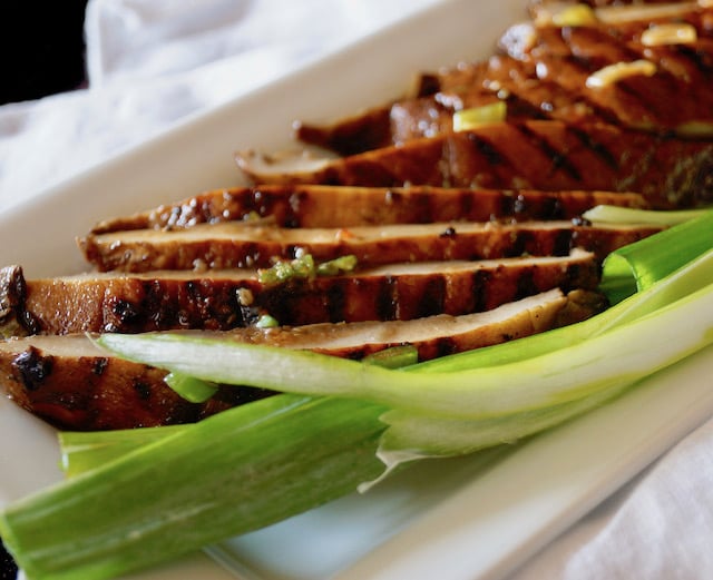 Sliced Marinated Grilled Portabello Mushrooms on a white plate with green onions.