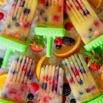6 orange popsicles with fresh berries inside, on crushed ice with berries