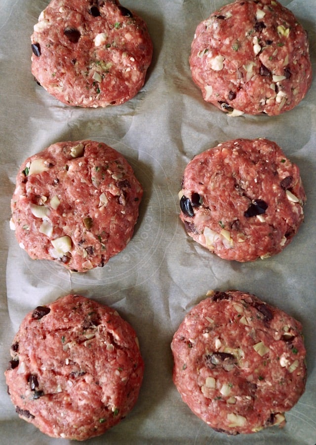 Six shaped, raw Mediterranean Burger on parchment paper.