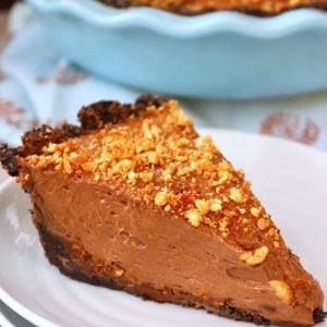 One slice of Nutella Pie topped with hazelnut praline on a white plate with whole pie behind it.