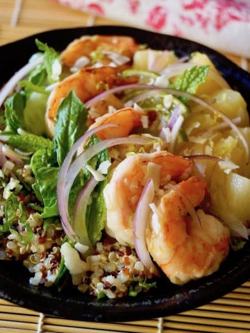 Tropical Quinoa Salad Bowl with Shrimp in a dark ceramic bowl on a sushi mat