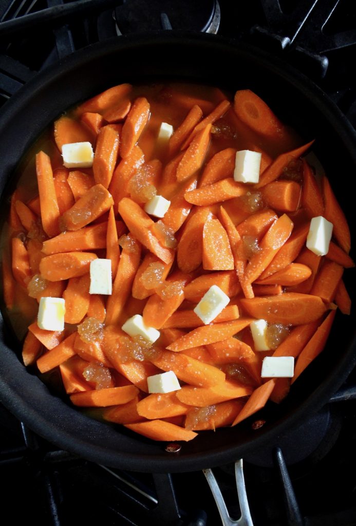 sliced carrots in saute pan with pieces of butter on top