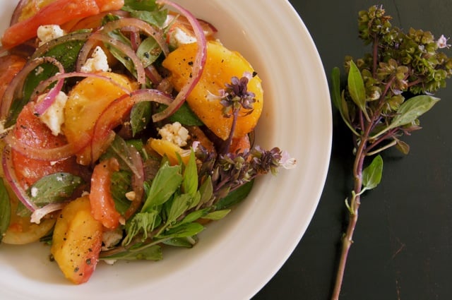 red and yellow tomato salad with Thai basil flowers in a white bowl