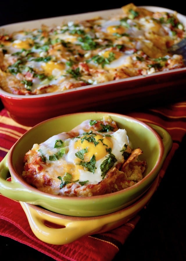 One serving of Chipotle Breakfast Nachos with Eggs in a green bowl with the baking dish behind it.