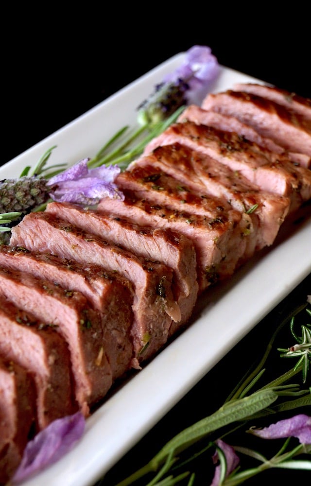 Sliced Lavender-Rosemary Grilled Ribeye Steak on a narrow white platter with fresh herbs.