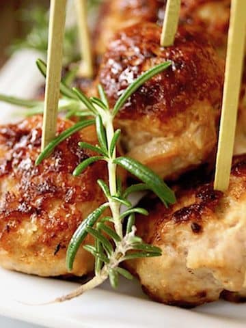 Rosemary Turkey Meatballs with Honey on a narrow white plate with toothpicks in each one.