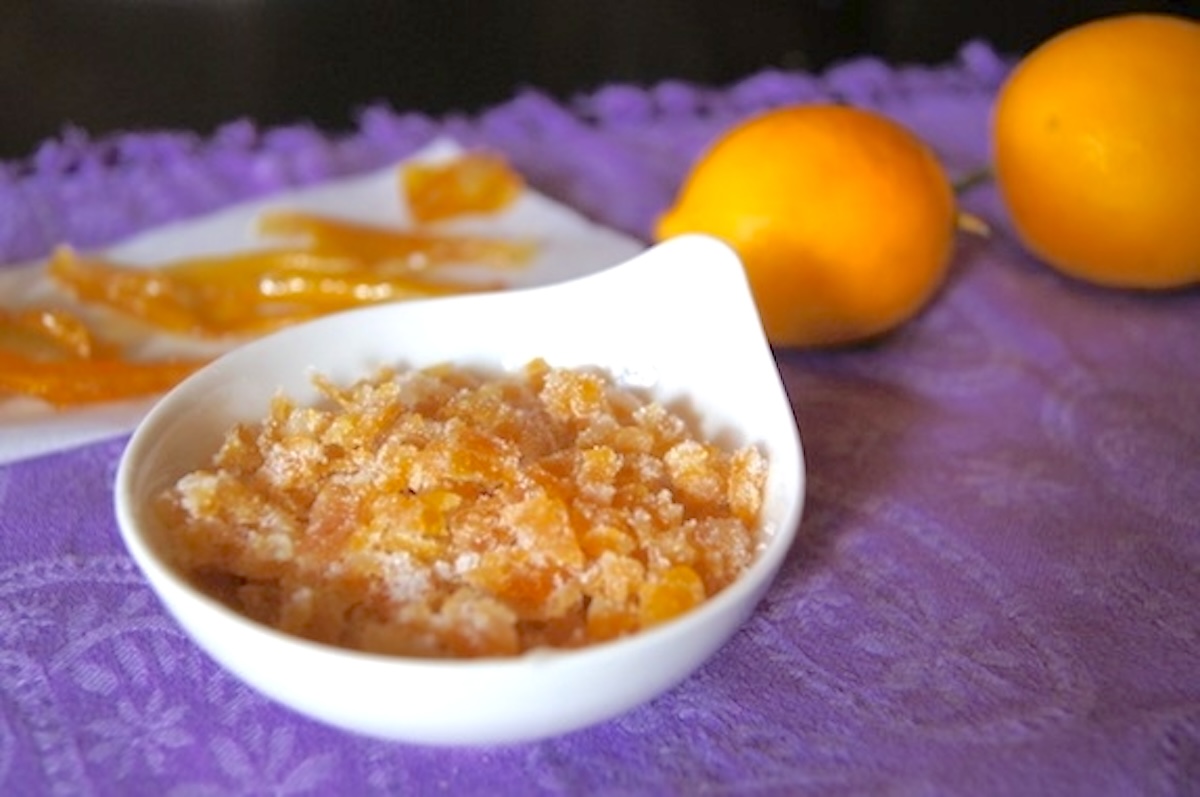 Candied-Citrus-Peels Candied lemon peels cut into strips and some chopped finely in a small white bowl, with two whole lemons next to them.