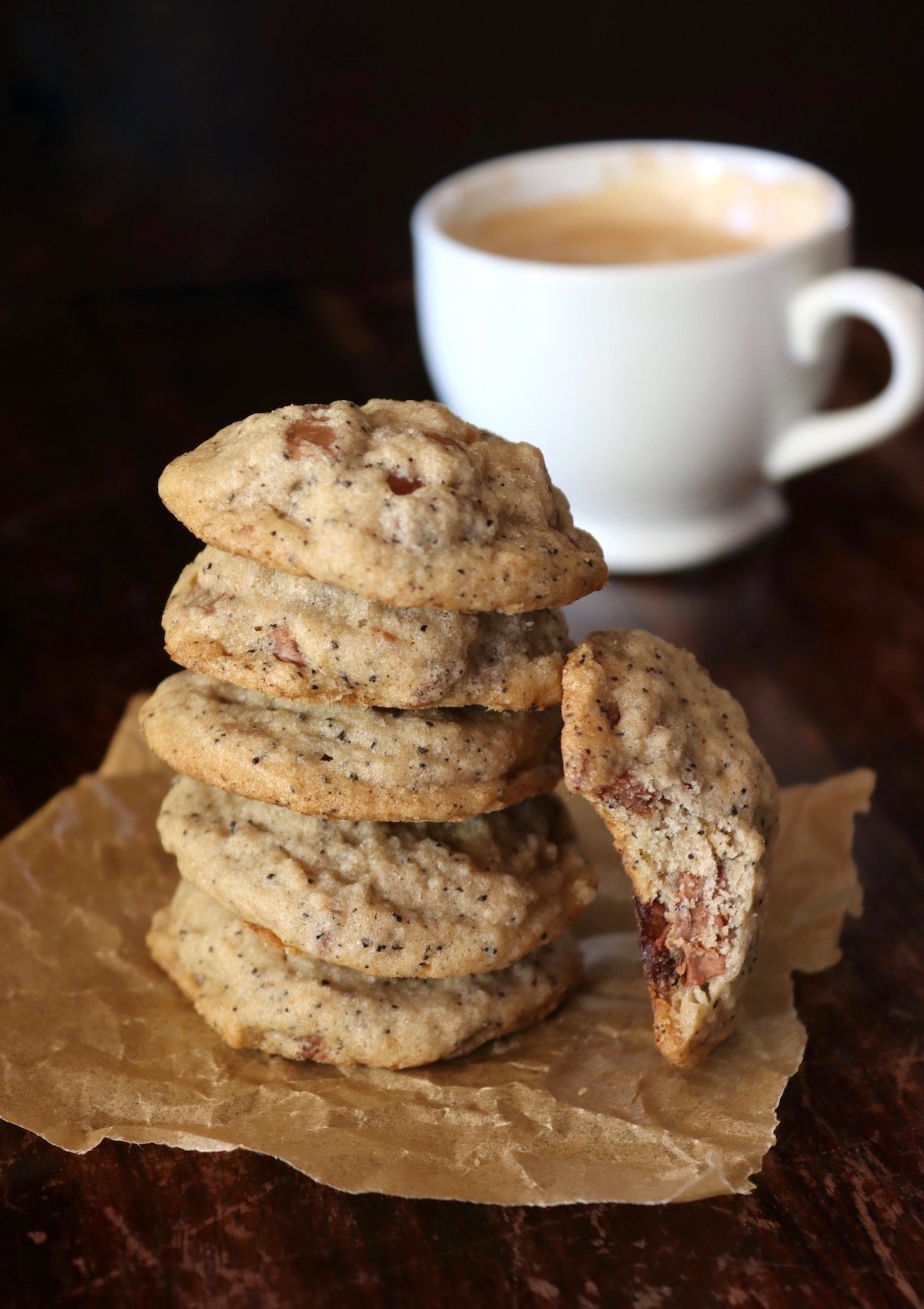 5 coffee chocolate chip coookies in a stack with one leaning on it with a bite taken out of it and white coffee mug behind them.