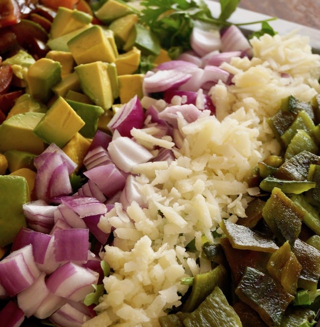 Rows of avocado, red onion, manchego cheese and roasted pobalnos for Mexican chopped salad with pepitas