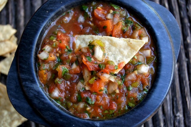 Roasted Tomato poblano Salsa in black bowl with a chip on top