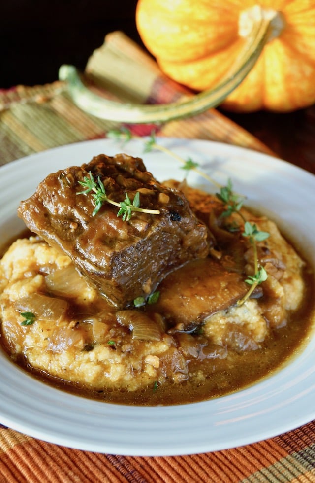 One serving of Pumpkin Braised Short Ribs on a bed of polenta with pumplin in background