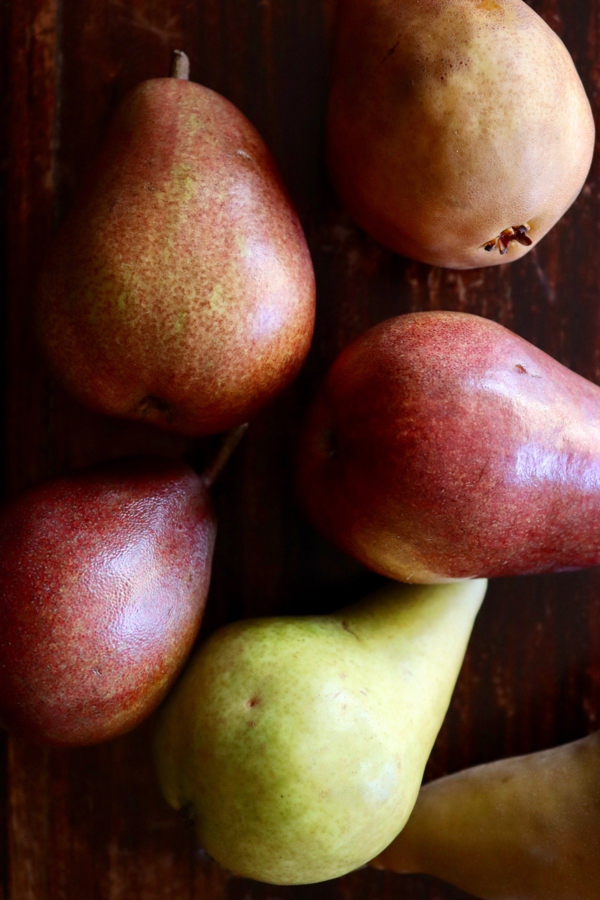 red, rust-colored and green pears of dark wood table