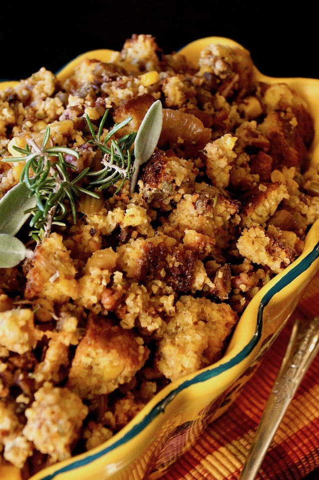 Gluten-Free Cornbread Stuffing in a yellow-gold dish with rosemary and sage sprigs