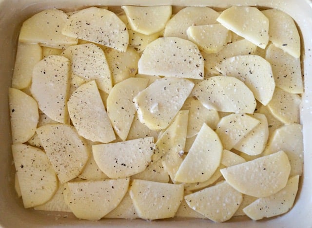 Layers of raw potato slice in baking dish for gratin