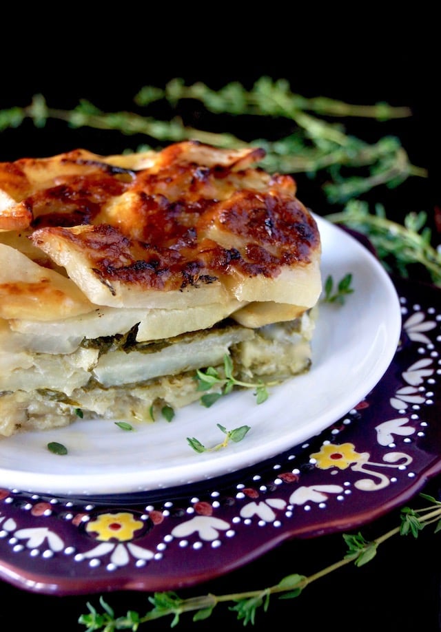 1 serving of Gruyere Spinach Potatoes Au Gratin on a white plate surround by fresh thyme sprigs.