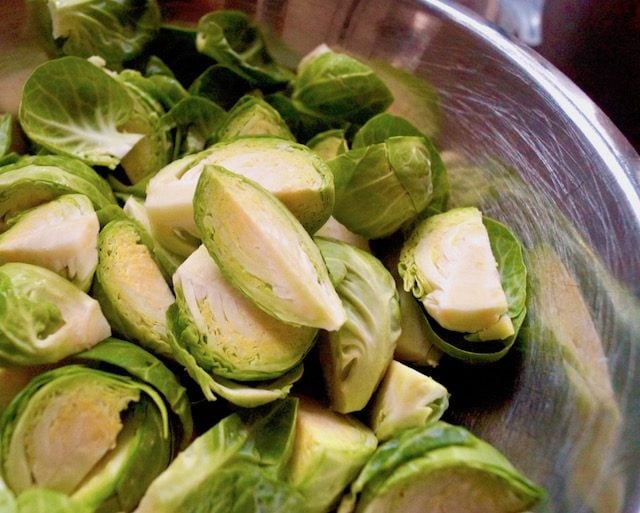 quartered, raw brussels sprouts in stainless steel bowl