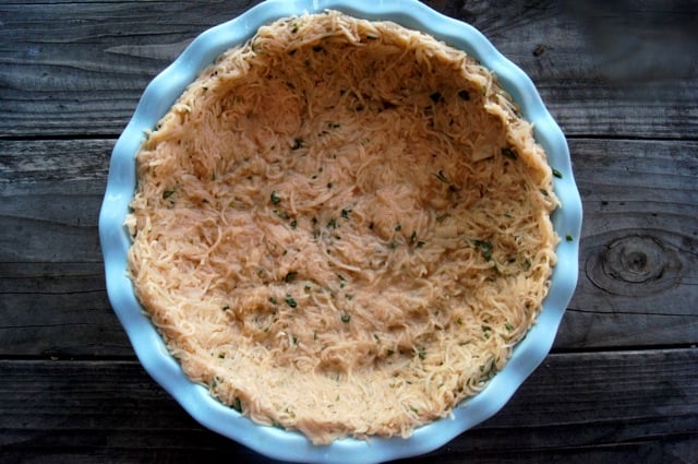 Raw potato crust in a light blue pie plate, ready to be baked. 