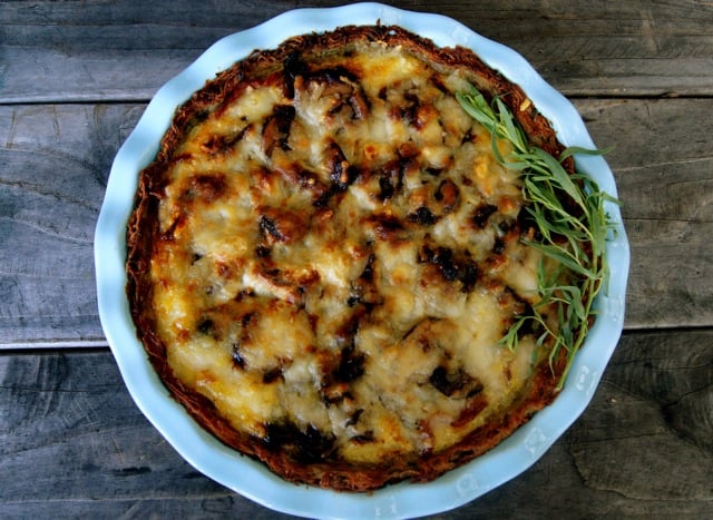 Mushroom Bacon Savory Pie with Potato Crust in light blue pie dish on a wooden background with fresh tarragon.