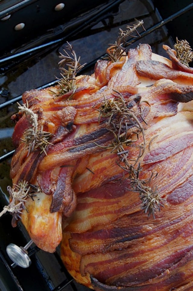 Crispy bacon wrapped around a roasted turkey with rosemary sprigs.