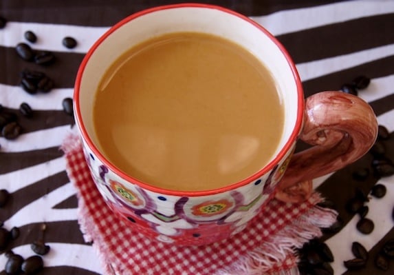 Coffee in a pretty painted mug on a red checked cloth with coffee beans.