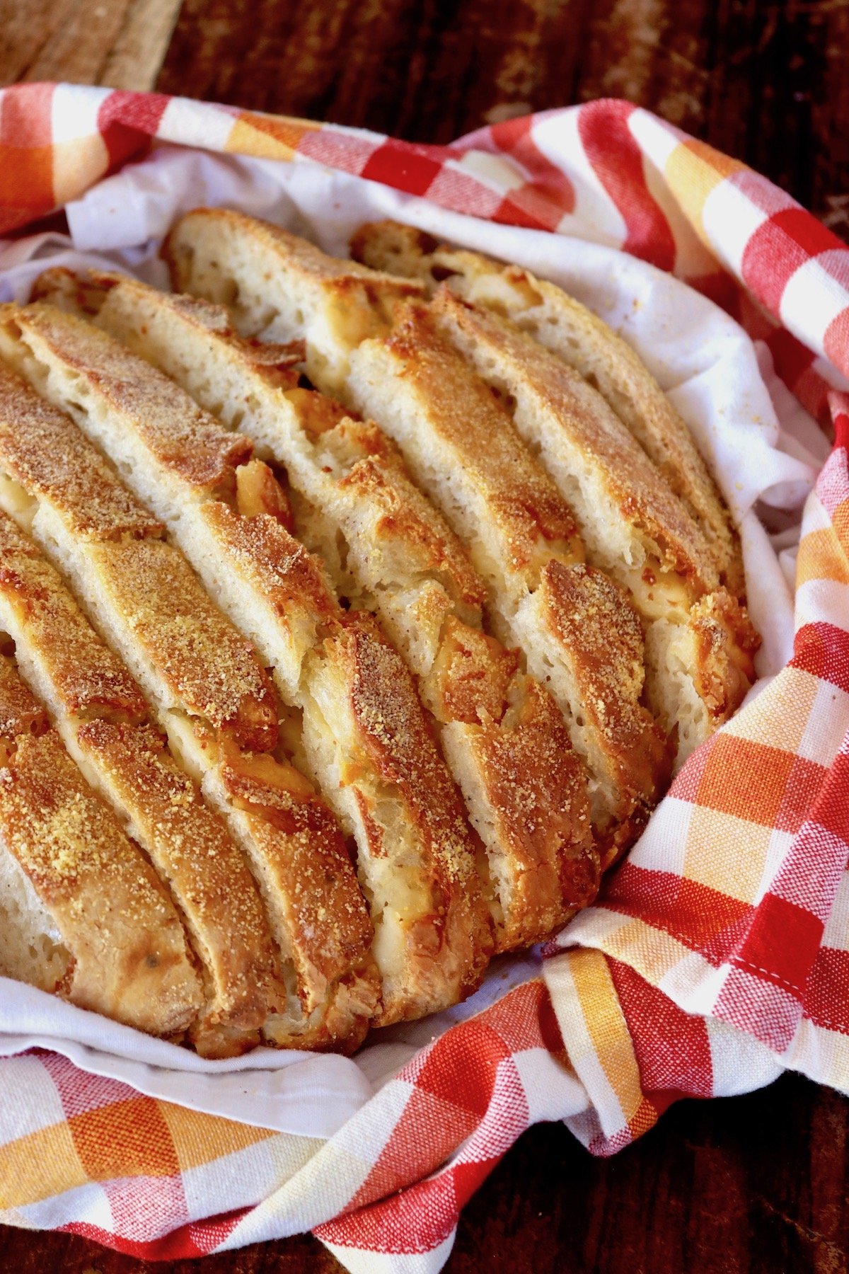 Whole, sliced golden loaf of Asiago cheese bread in a red, orange and white checkered cloth.