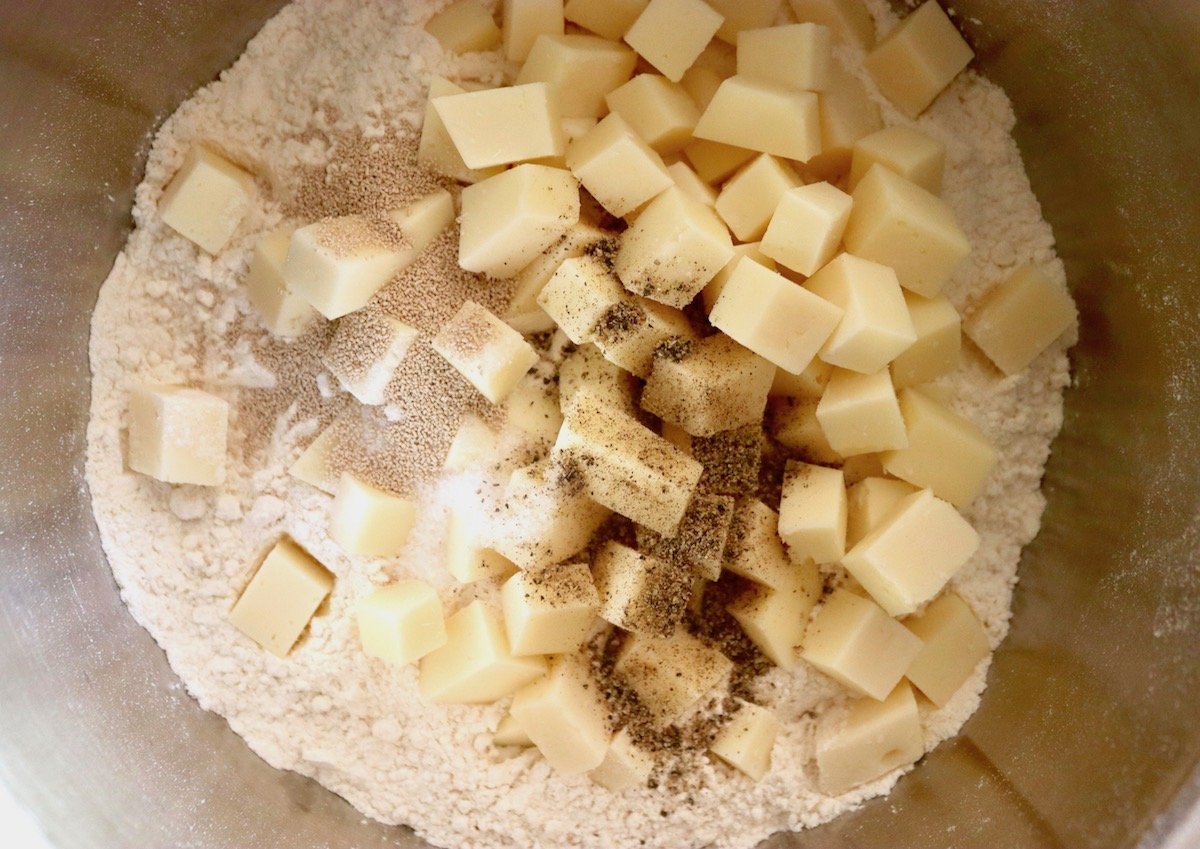 Bowl filled with flour, yeast, salt, pepper and cubes of Asiago cheese.
