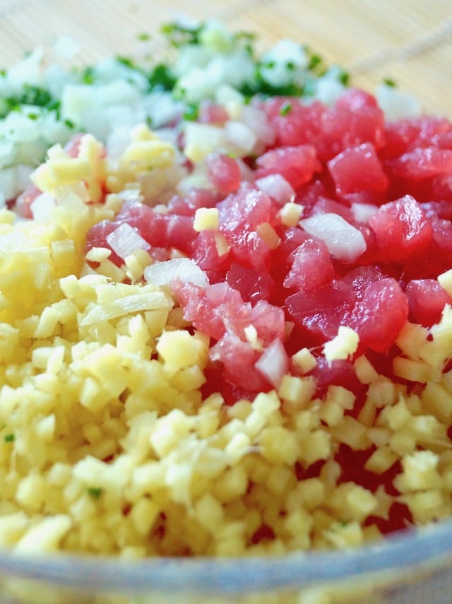 close up of super finely chopped ginger, ahi tuna, white onion and chives, in a glass bowl.