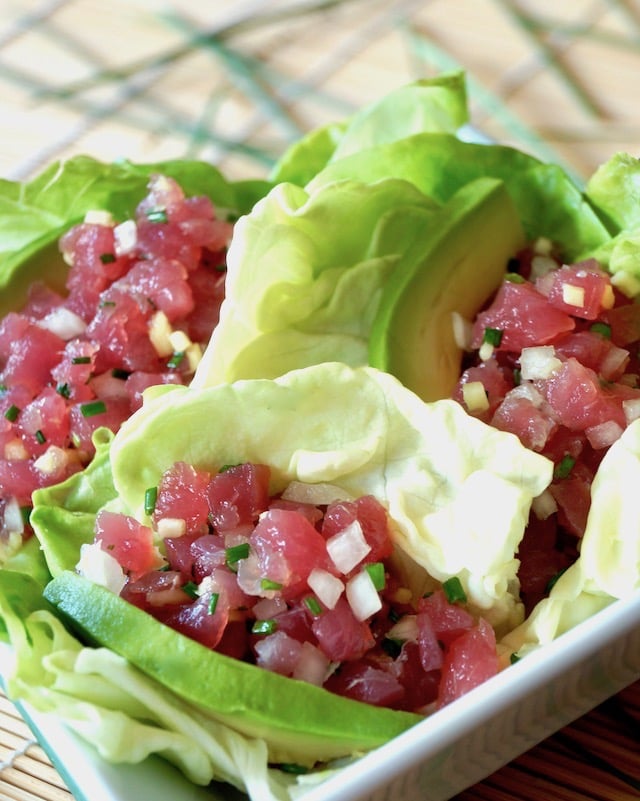 Ahi tuna tartare in butter lettuce cups with avocado slices on a sushi mat.