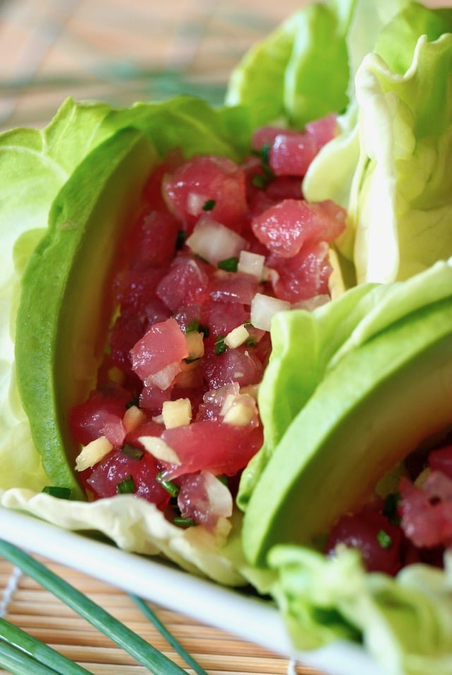 Ahi tuna tartare in butter lettuce cups with avocado slices on a sushi mat.