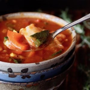 Three ceramic stacked bowl with the top one full of tomato fish stew, with one bite in a spoon.