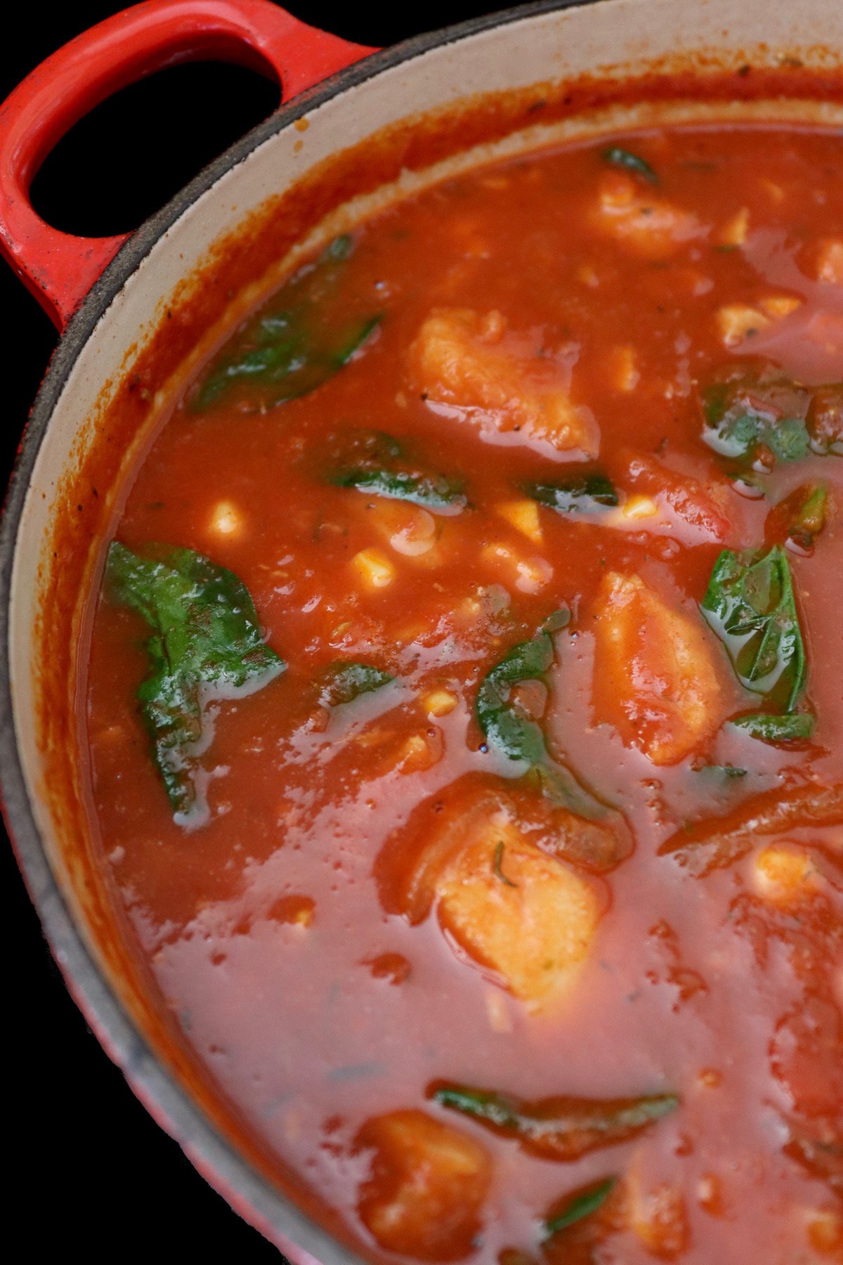 big red pot ful of tomato fish stew with spinach leaves.