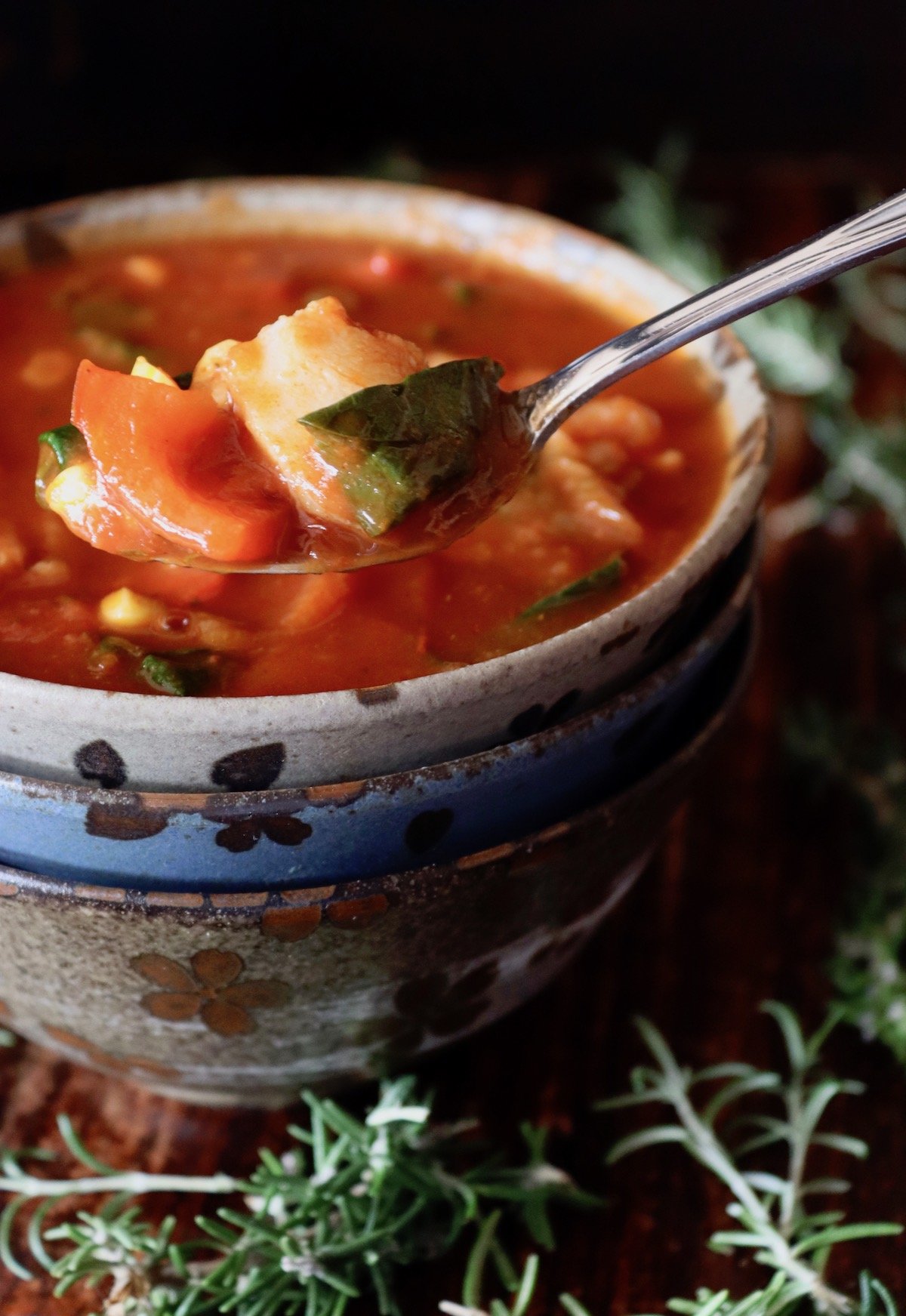 Three ceramic stacked bowl with the top one full of tomato fish stew, with one bite in a spoon.