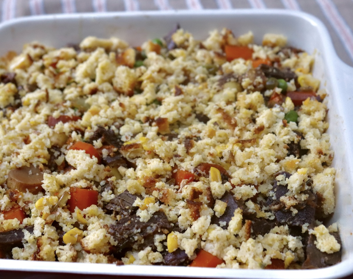 Braised-Brisket-Casserole Beef brisket stew in a casserole dish, topped with cornbread crumbs.