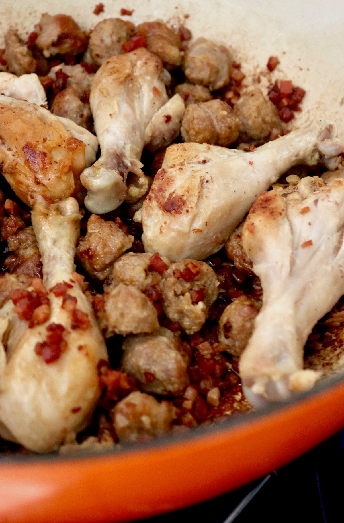 browned drumsticks, sausage and pancetta in pot