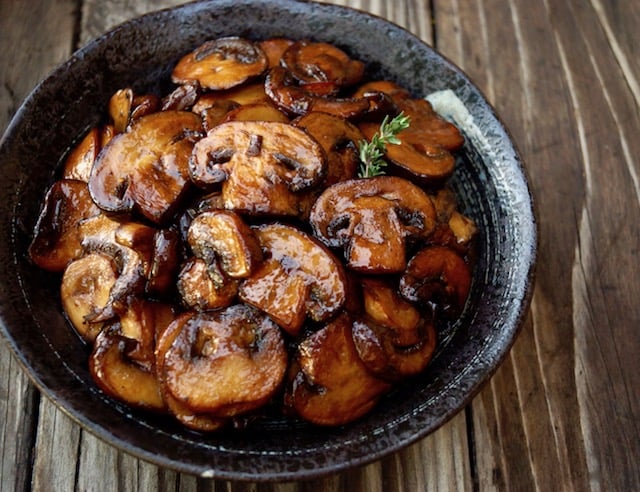 browned mushrooms in black bowl on wood surface