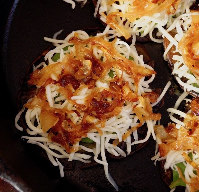 Portobellos with cheese and onion in black pan.